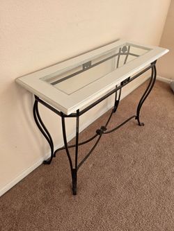 This white-painted console table features a glass top insert and curved black wrought-iron legs with