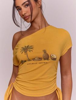 Yellow one shoulder crop top with graphic of palm tree, pineapple, and coconut with the words 'LOCALLY GROWN