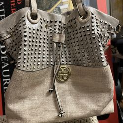 Fashion tote handbag. It's a light beige color with a gold logo and a drawstring closure.