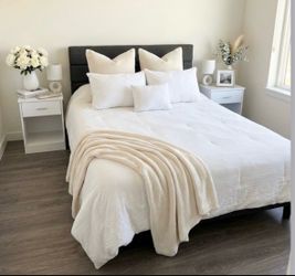 Español: Cama con cabecera gris, dos mesas de noche y dos lámparas. English: Bed with gray headboard, two nightstands, and two lamps.
