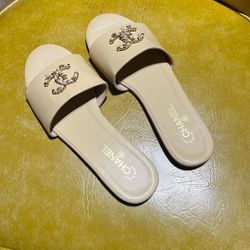 Beige slide sandals with a gold embellished double-C logo on the front strap