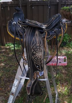 Western-style black leather saddle with extensive hand tooling, plus stirrups and rigging