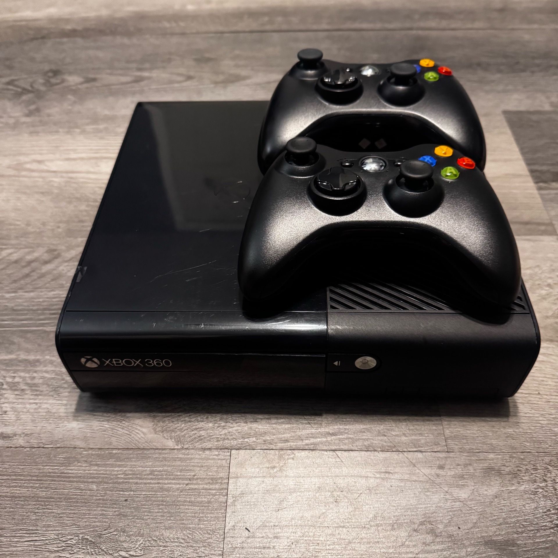 Black Microsoft Xbox 360 E console bundled with two matching wireless controllers