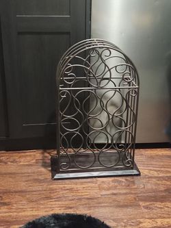 vintage free-standing scrollwork metal wine rack with an arched top, featuring a dark or oil-rubbed bronze finish and an open circular lattice design 