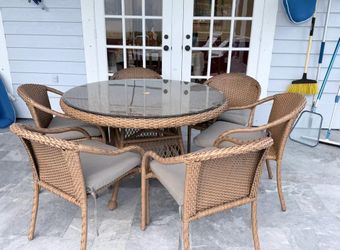 Outdoor wicker dining set with large round glass-top table and 6 matching armchairs.