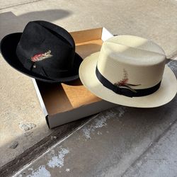 Two fedora hats, one in black wool felt and the other in natural straw, both featuring a grosgrain ribbon and a feather