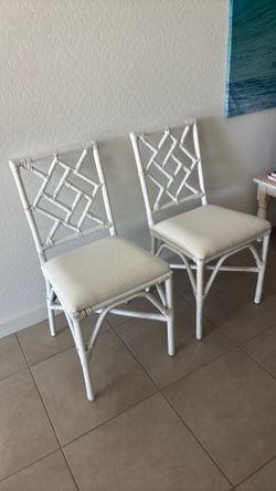 Two white rattan chairs with attached cushions