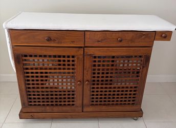 CABINET Multi-purpose storage with swivel wheels,  built-in fold-out ironing board, 2 drawers, and spacious shelving behind double doors. Perfect for 