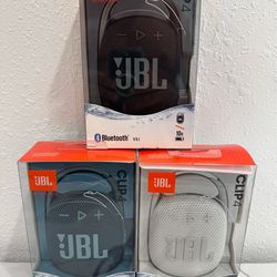 New JBL Clip 4 portable speakers in black, blue, and white. Each unit has a built-in carabiner for easy attachment. These speakers have Bluetooth 5.1 