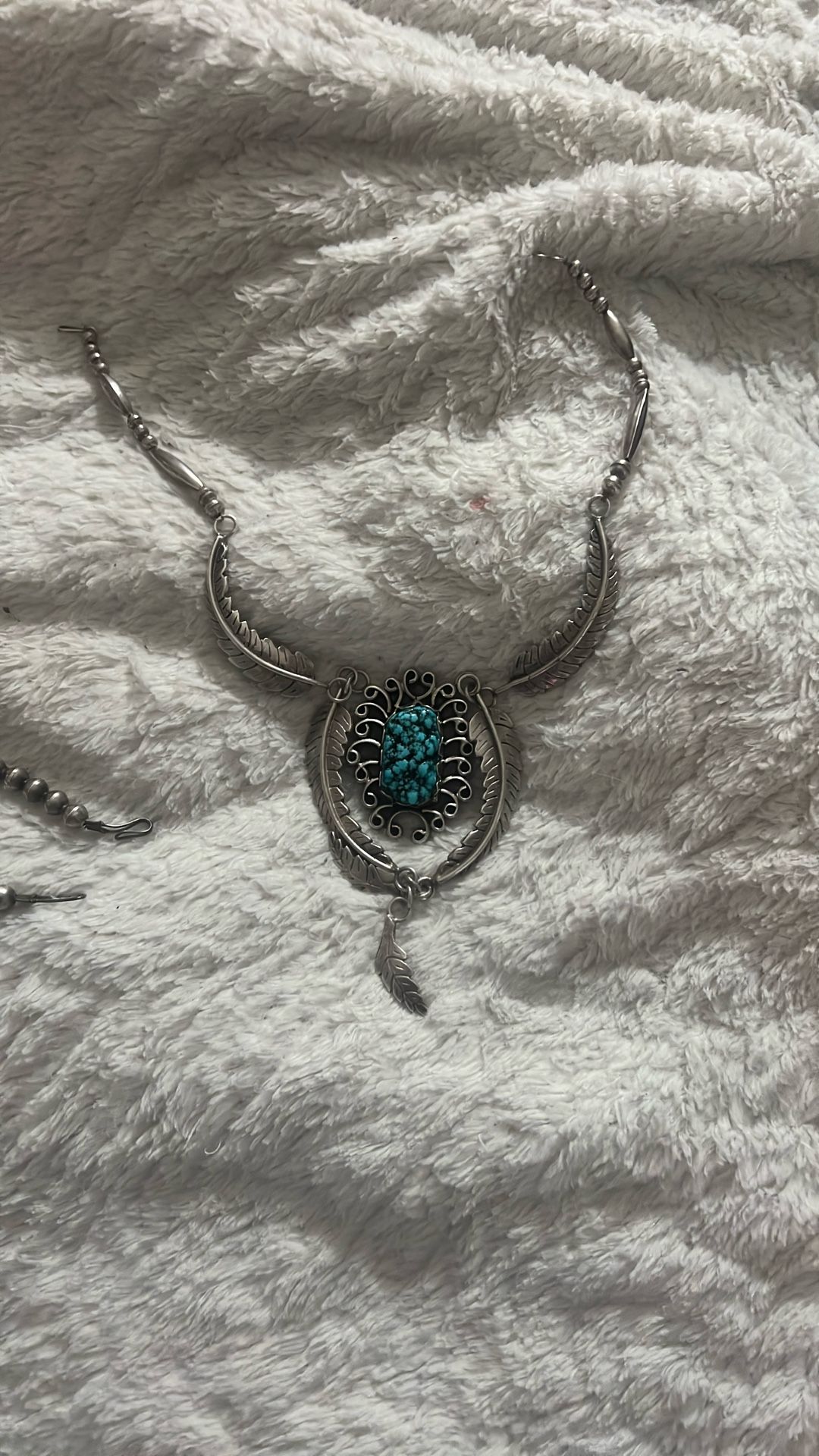 This necklace is a Southwestern or Native American-style silver and turquoise necklace featuring prominent feather and scroll motifs. It combines elem