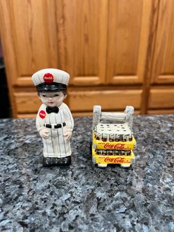 Ceramic Coca Cola Delivery man and Cart of Bottles pair of Salt and Pepper Shakers. Size delivery man approximately 4 inches tall. Preowned never u