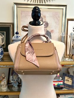 Catherine Malandrino's taupe handbag features a grainy texture and a decorative scarf on the handle.