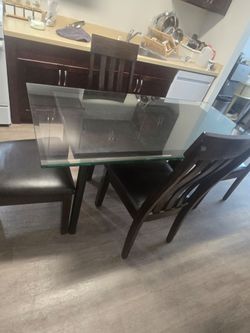 Modern dining set features a dark wood frame with a rectangular glass tabletop and chairs upholstere.