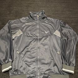 Nike track jacket. It's a dark gray model with reflective details and a full-zip closure. Product Details Brand: Nike Color: Dark gray Features: It fe