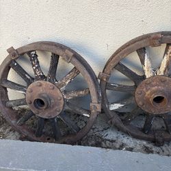 Two rustic, timeworn wagon wheels with corroded iron rims and sun-bleached wooden spokes