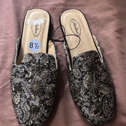 Atalina women's mules feature a black Paisley patterned fabric upper adorned with rhinestones and decorative rivets.