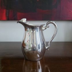 Vintage silver-plated water pitcher with scrolled handle and ice lip.