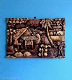 Vintage hand-carved wood panel depicts a traditional village scene palm trees