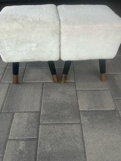 2) white faux-fur square ottomans  black legs with distinctive gold-capped feet.