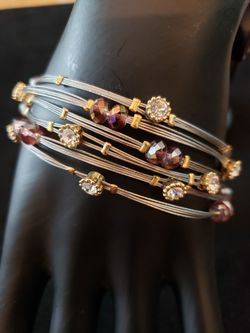 Six wire bangle bracelets never worn. Has rhinestones and purple glass beads on each.