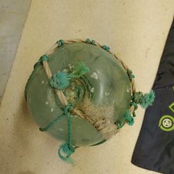 hand-blown dark green glass buoy encased in a rope Net