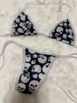 Two-piece string bikini with black fabric and white skull print. White trim and adjustable tie straps. Bold, edgy graphic look. Lightweight swim or be