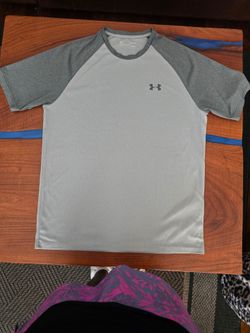 Under Armour athletic tee in light gray with darker gray raglan sleeves. Breathable, quick-dry fabric for workouts. Crew neck with subtle UA logo on c