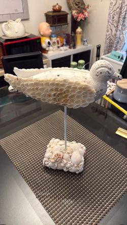 A decorative carved wooden bird sculpture with seashell accents on a base.