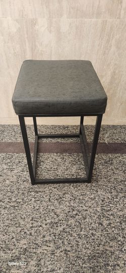 square bar stool with a gray upholstered seat and black metal frame. 