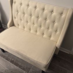 Cream/Ivory upholstered bench with a tufted back and winged sides.