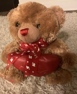 Brown teddy bear holding a red heart that says "Love."