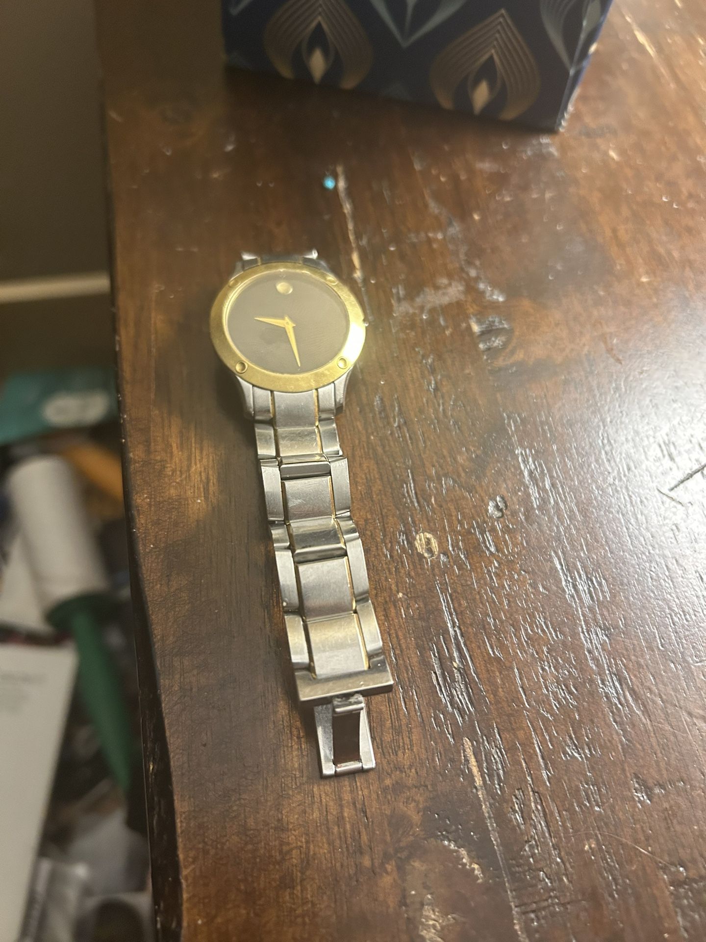 Movado two-tone stainless steel wristwatch with a gold-plated bezel and a black dial. It features the brand's signature single gold-toned dot at the 1