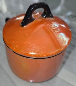 Vintage lusterware covered handled soup mug, orange exterior with black handle and lid knob, iridescent pearl‑glaze interior. Measures 3"D x 4"H. Good