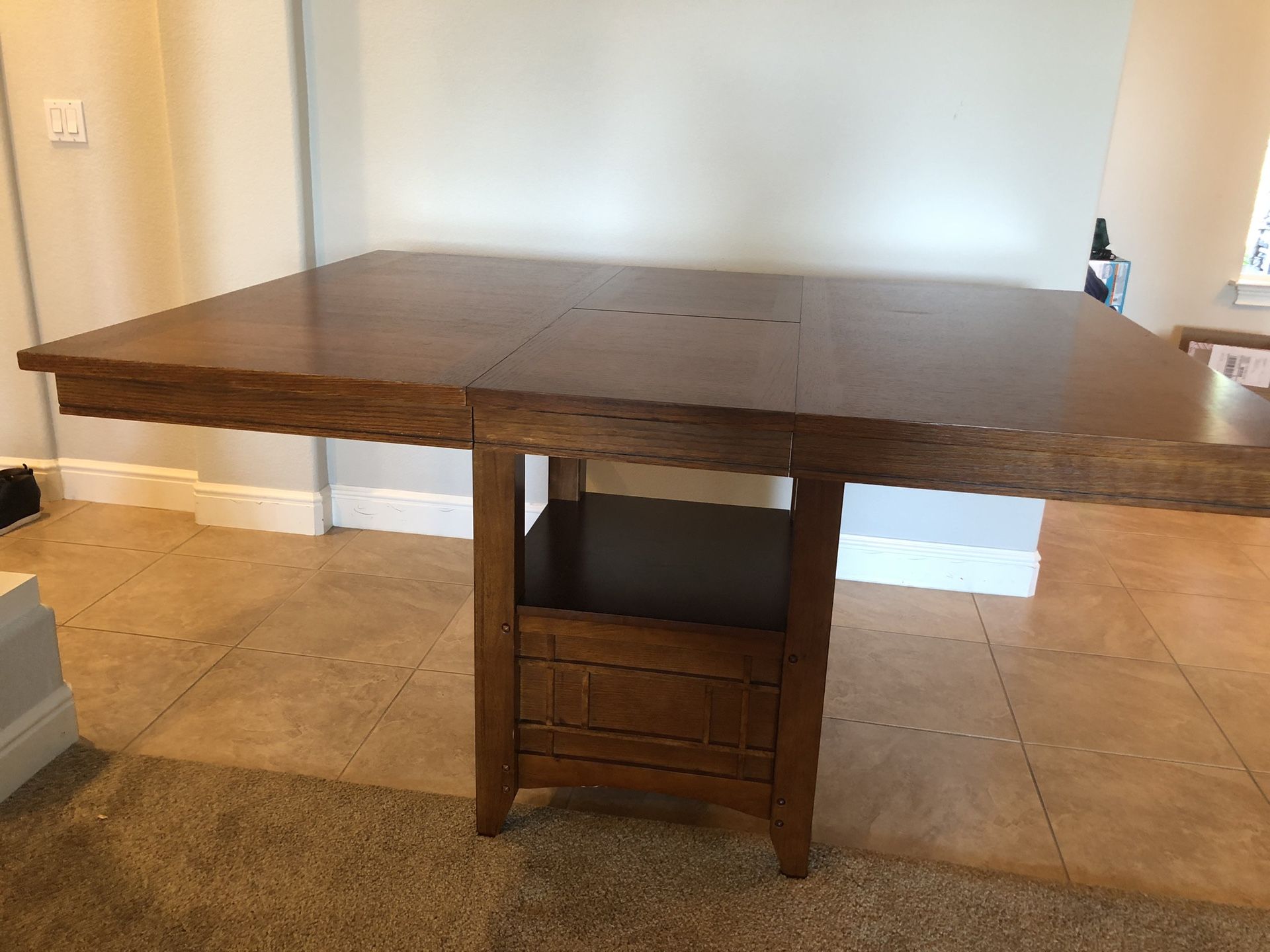 Bar height wood dining table. Can be square 48”x48” or rectangle with a middle leaflet. It has a storage and shelf under and is used but as good as n