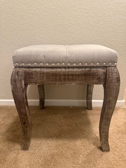 Vanity stool/accent bench featuring neutral linen-look fabric and distressed wood.
