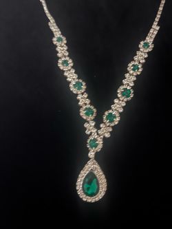 Elegant necklace has a series of round green stones set in floral-shaped links. The piece is centered by a large teardrop-shaped green pendant surroun