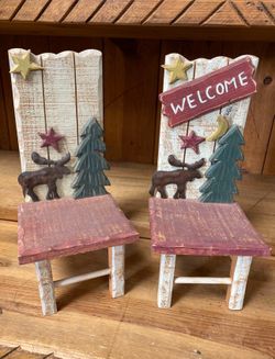 These rustic decorative chairs feature handmade wood construction with a "WELCOME" sign, moose, pine tree, and star cutouts.The items are styled for c