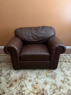 Oversized  brown leather armchair features classic rolled arms and a plush, pillow-top back cushion.
