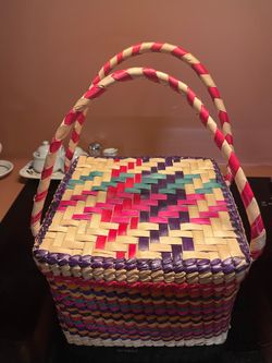 Handwoven palm straw basket with a removable lid and a geometric pattern in pink, purple, and teal