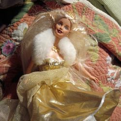 The doll wears a lavish gold gown with a backless bodice and vertical stripes of silver, accented with silver snowflakes. 
It features a white faux fu
