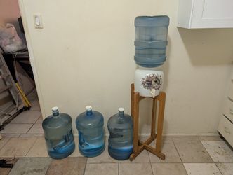 Water dispenser, stand and three full 5-gallon bottles