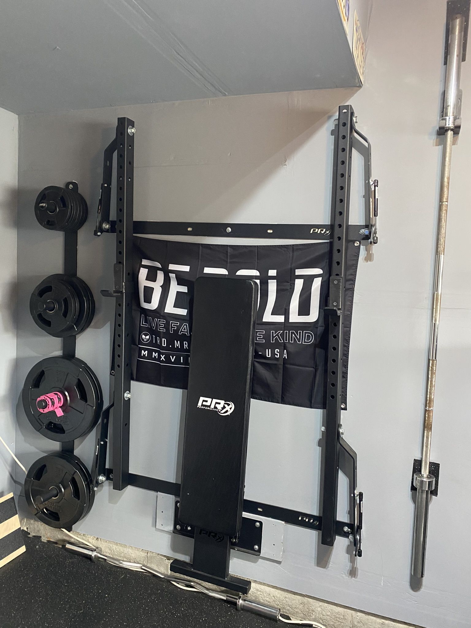 RX Profile ONE Folding Squat Rack with rstorage accessories, barbell and rubber grip plates.