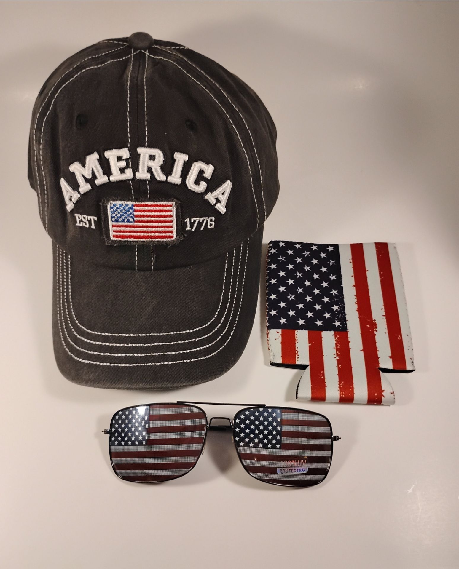 America Est 1776 baseball cap with adjustable strap. A pair of American flag sunglasses and can coozie also included.