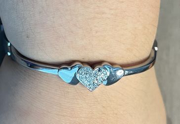 Elegant silver-tone bracelet featuring linked hearts and a central pavé crystal heart. Shiny silver finish adds classic shine. Perfect for everyday we