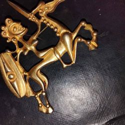 vintage brooch featuring a figure on horseback, possibly a knight or a warrior, holding shield&sword