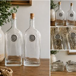 Set of 2 Decorative Glass Bottles with Cork Stoppers Beautiful matching set of 2 clear glass bottles. Each features a unique embossed medallion with a