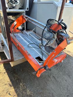 Diamond blade wet tole cutter saw Heavy-duty features an orange metal frame with a sliding motor assembly on dual chrome rails. This tool has a diamon