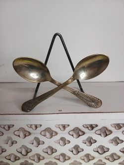 Anthropologie silver spoon holder, crafted from crossed vintage-style spoons, is designed as a decorative stand for napkins, plates, or artwork. 