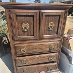 vintage Spanish-style armoire or chest of drawers featuring natural wood grains and ornate forged iron hardware. 