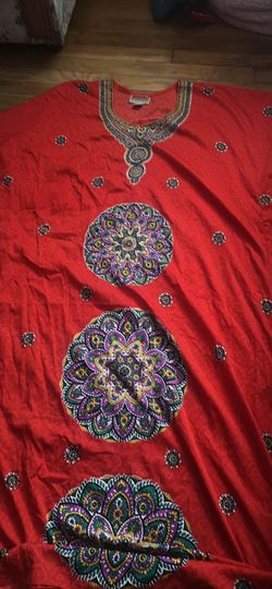 Vibrant red kaftan is made of a lightweight fabric with a silky sheen. It has a decorative embroidered neckline and three large, colorful mandala patt